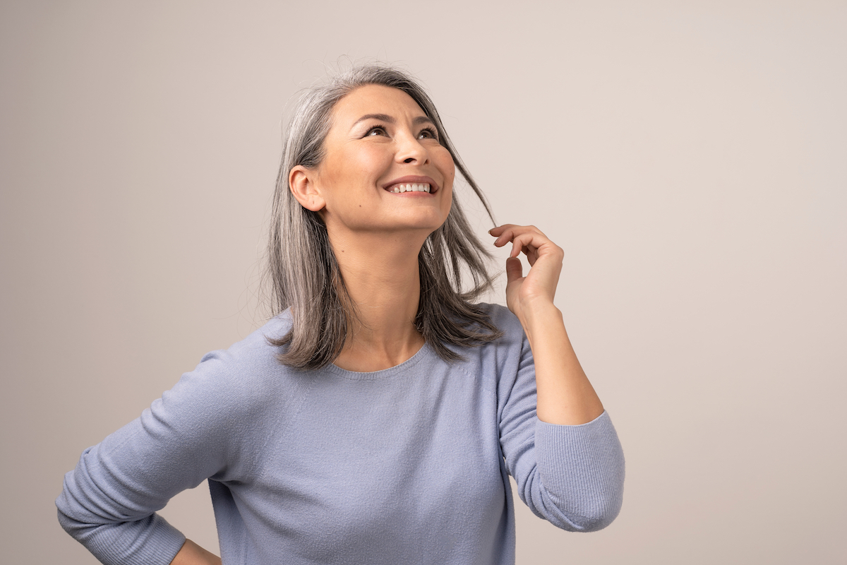 An attractive woman with gray hair wearing a lavender sweater looking up and smiling.