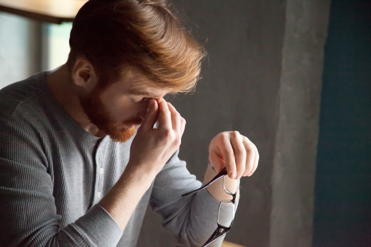 Tired red haired man take glasses off working too long at computer, exhausted millennial male suffer from headache or eye tension, young student massaging nose bridge feeling fatigue