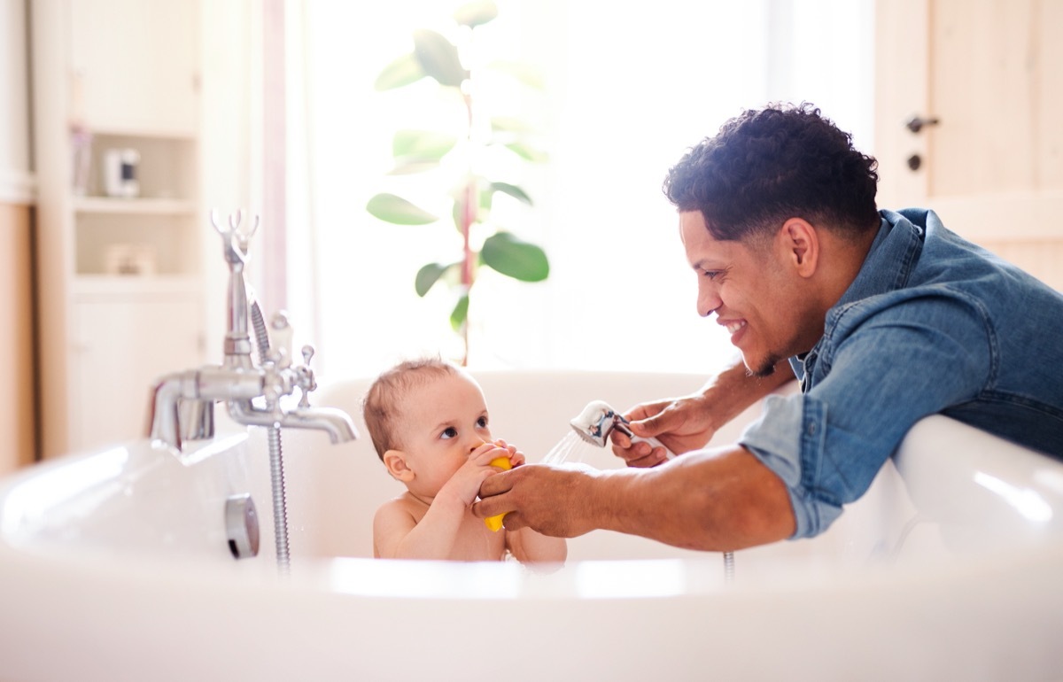 young man bathing baby in white tub