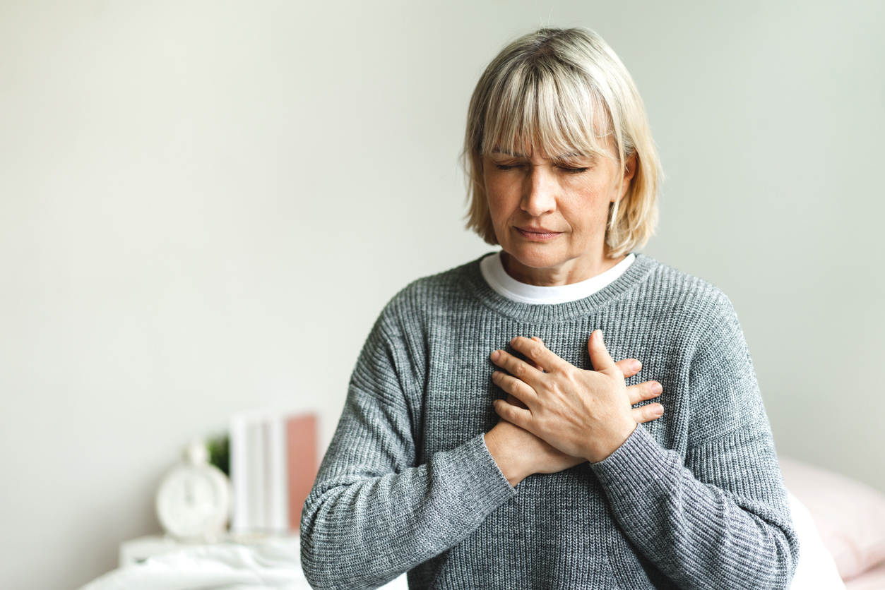 A woman holding her chest while sitting on her bed