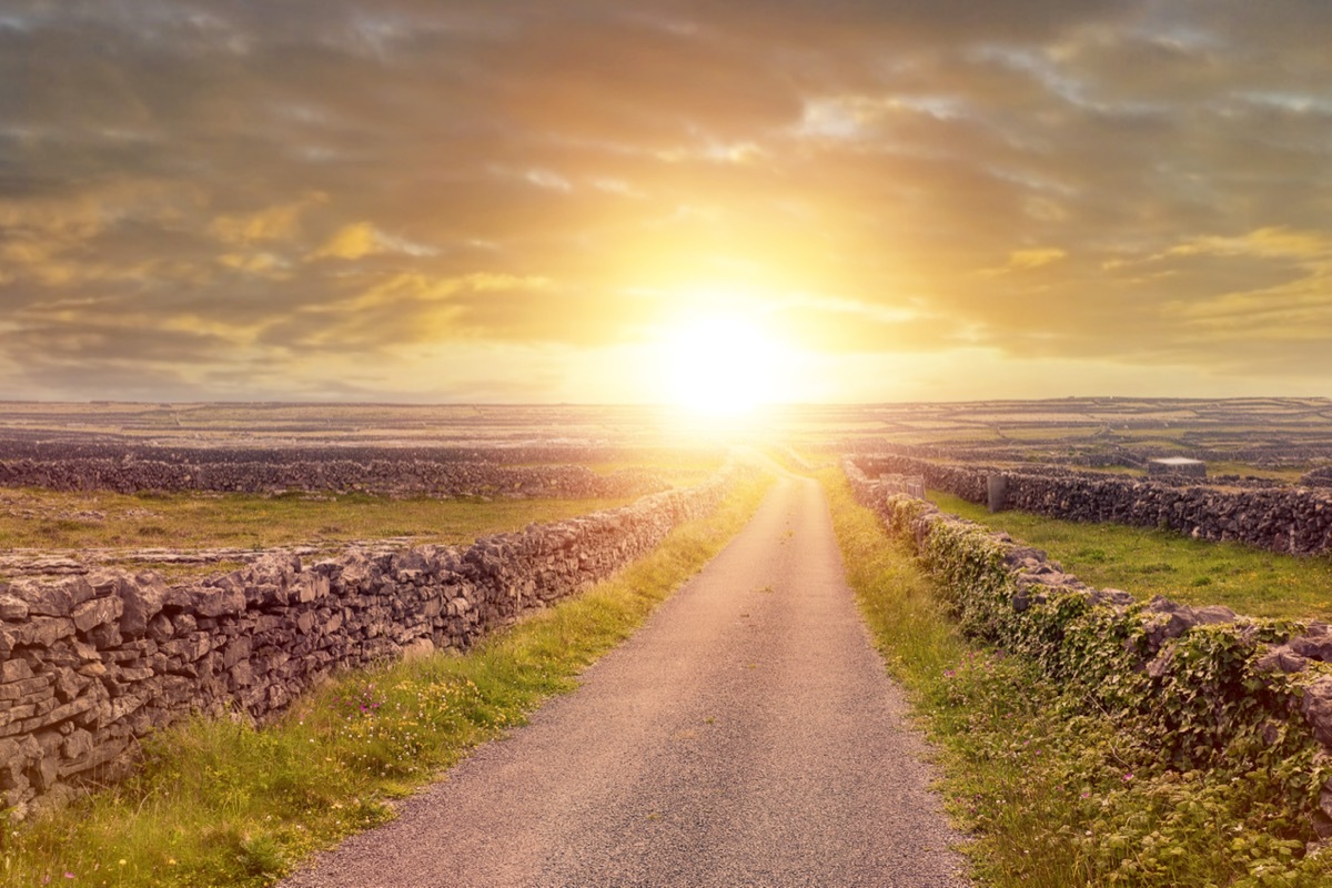 Small narrow country road with stone fences at sunset