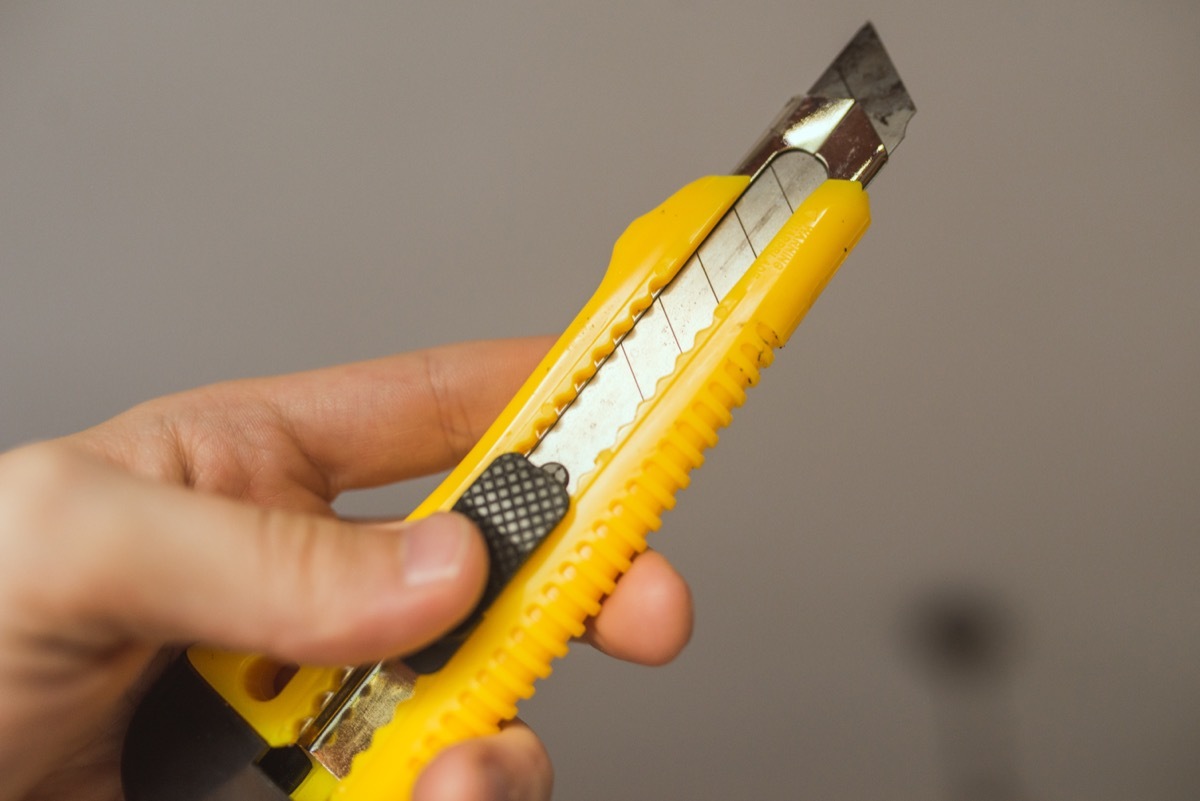 hand holding yellow box cutter tool