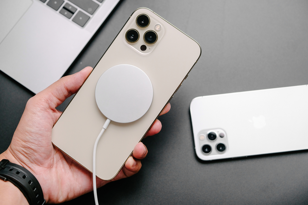 A hand holding an iPhone 12 that is hooked up to a MagSafe charging device