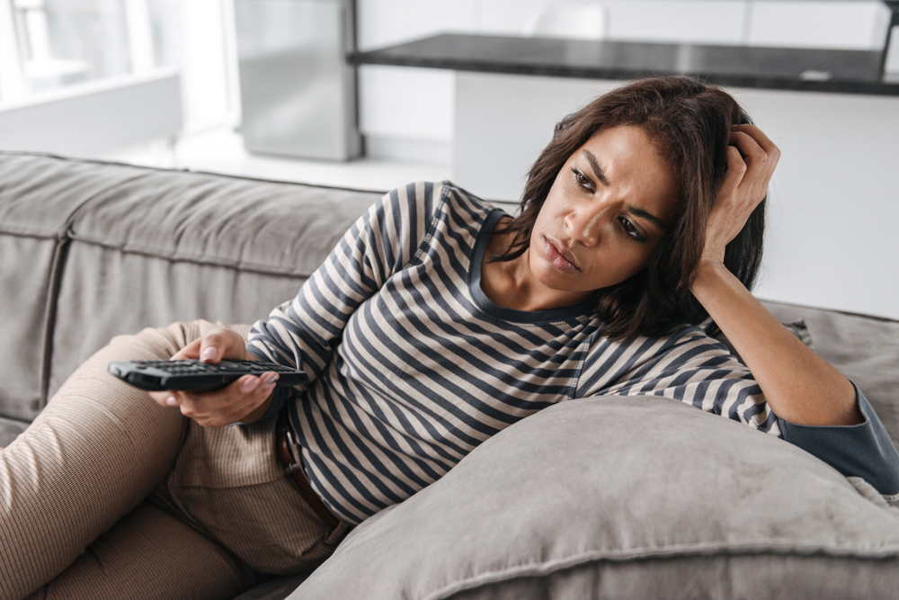 A young woman watching TV on the couch with a disappointed look on her face