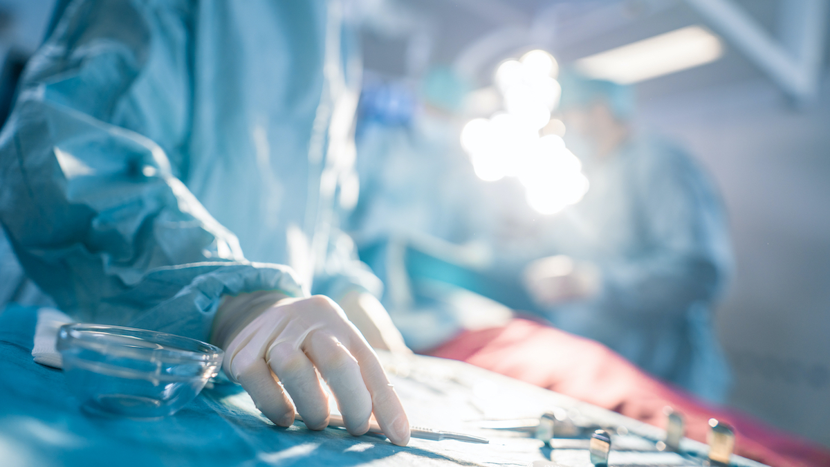 Close-up Shot in the Operating Room of Surgical Table with Instruments, Assistant Takes Instruments for Surgeons During Operation. Surgery in Progress. Professional Medical Doctors Performing Surgery.