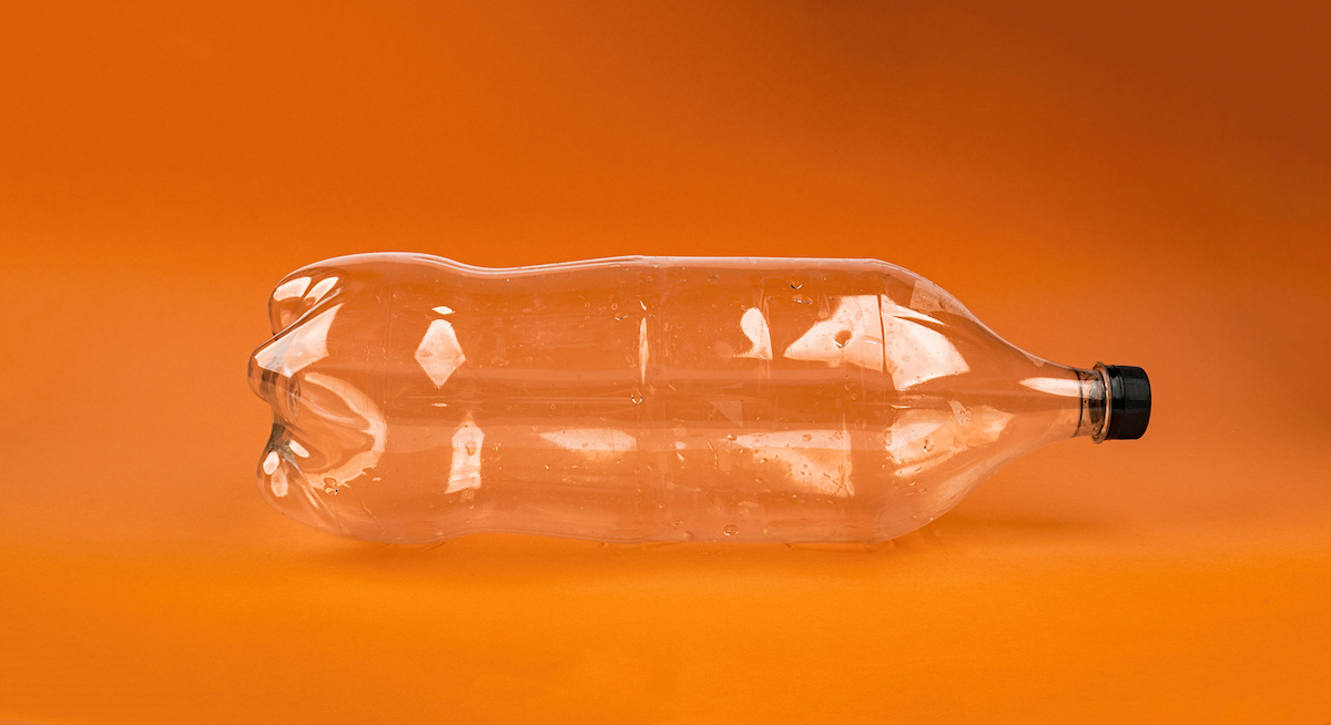 An empty clear two-liter soda bottle on an orange background