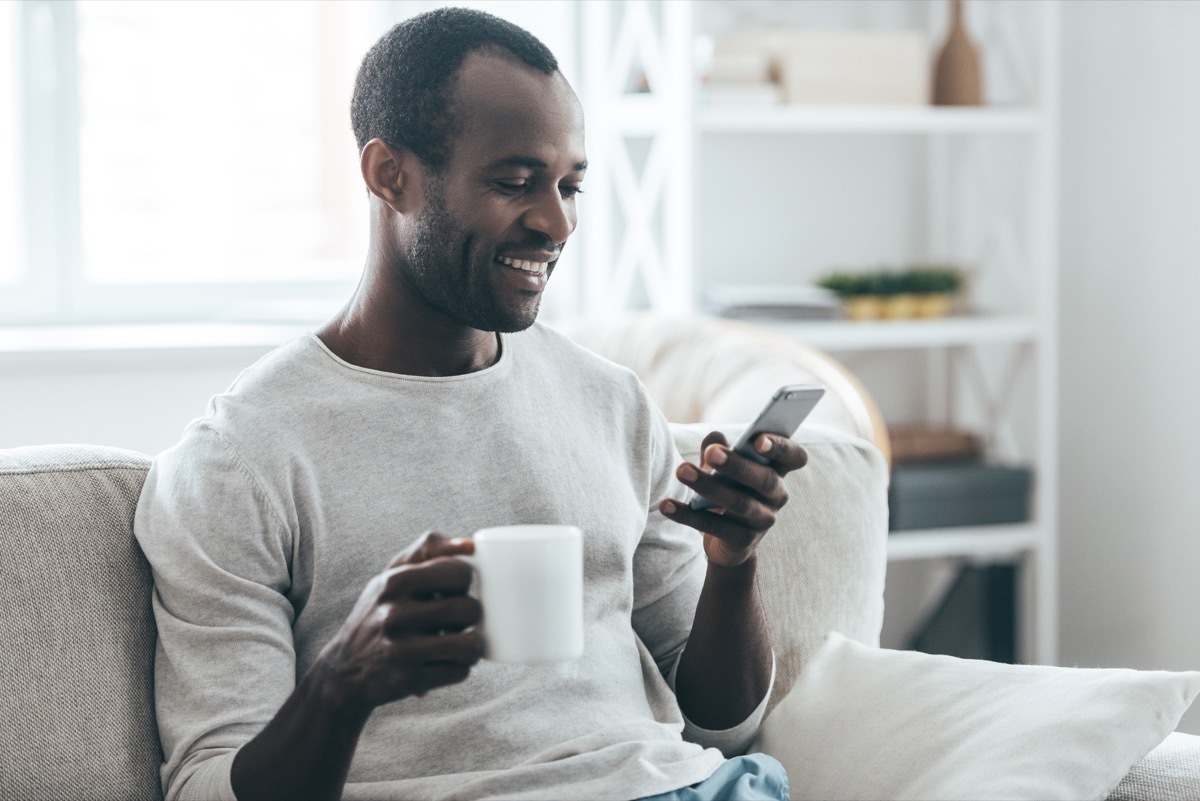 middle aged black man texting on couch with cup of tea