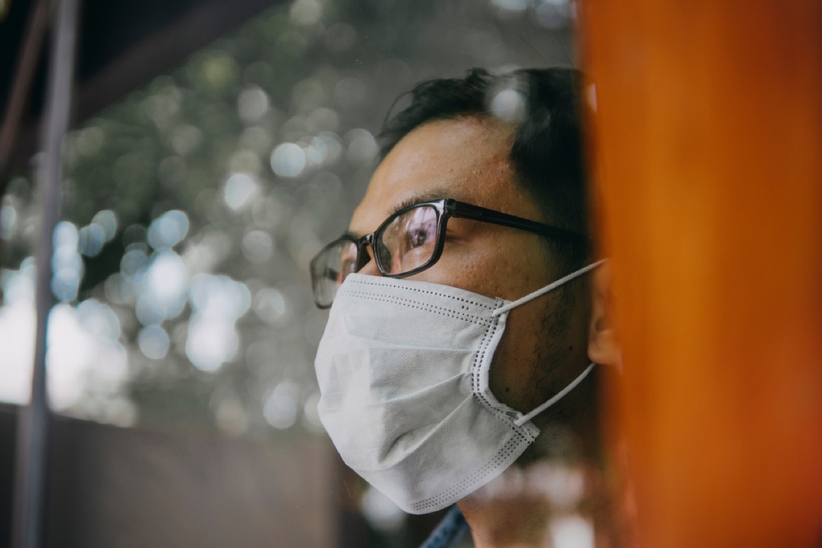 asian man with face mask looking out a window