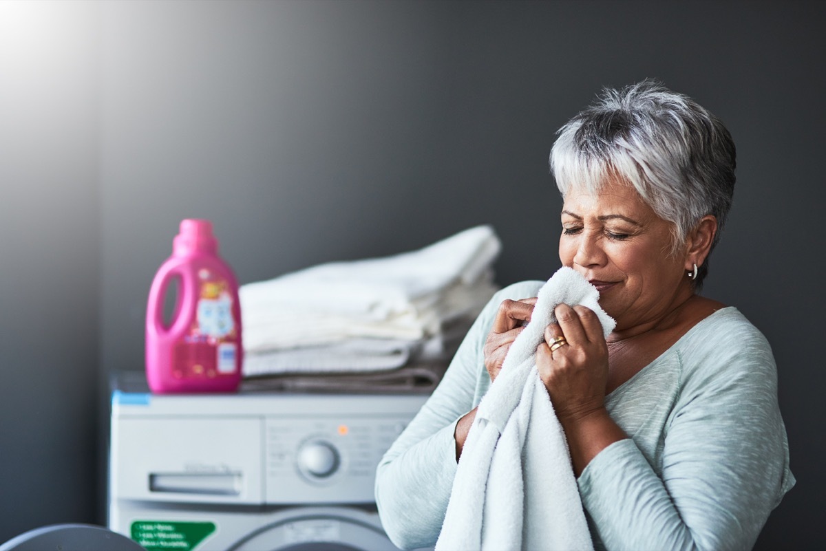 older latina woman smelling a fresh towel near the washing machine