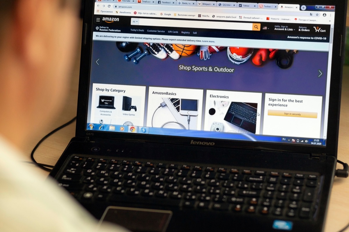 Russia, Samara, July 2020: A young man selects products online on the popular Amazon website on a laptop at night during the coronavirus epidemic.