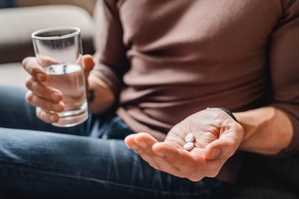 A person holding two pills in the palm of their hand and a glass of water