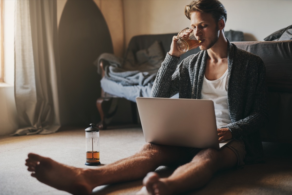 Shot of a handsome young man using his laptop while sitting on the floor at home