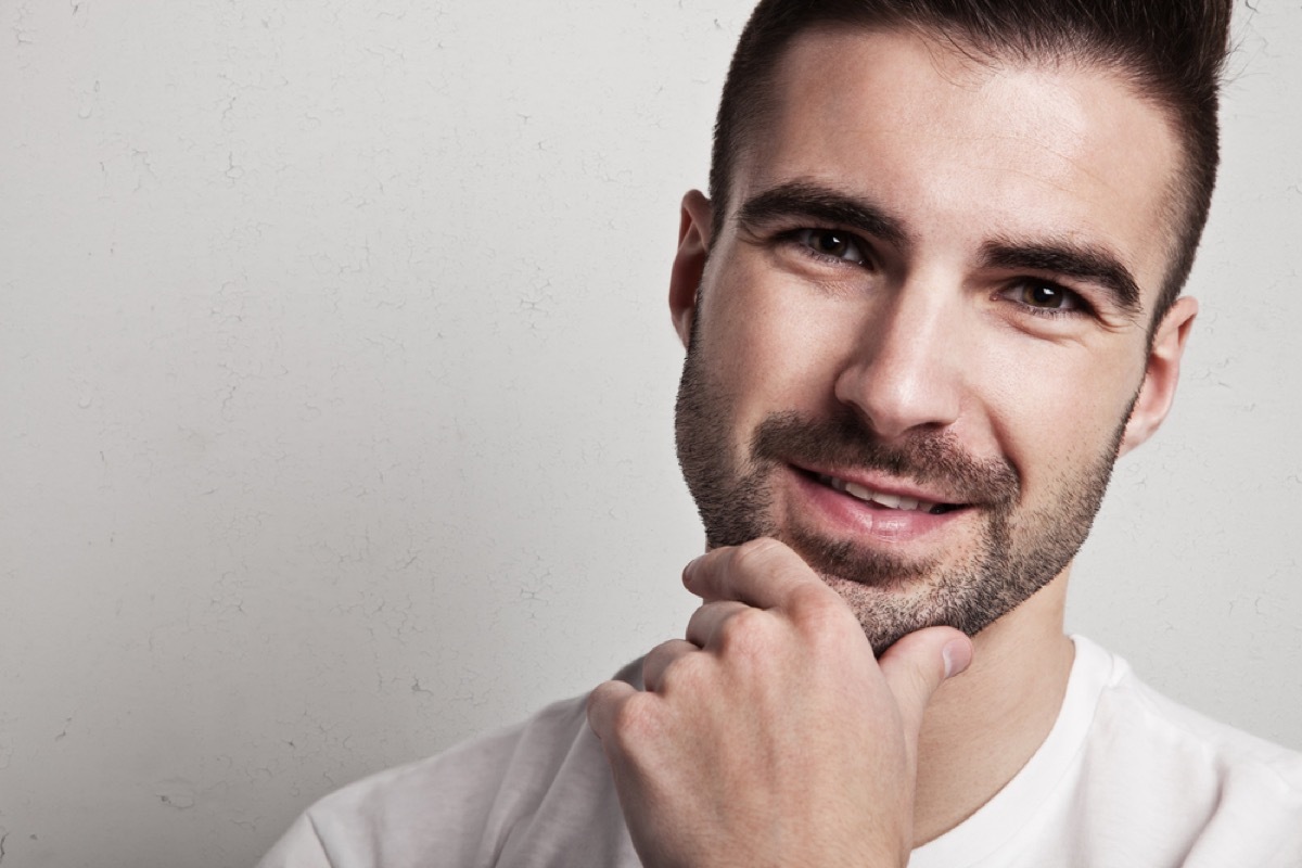 man with heavy stubble smiling with hand on chin