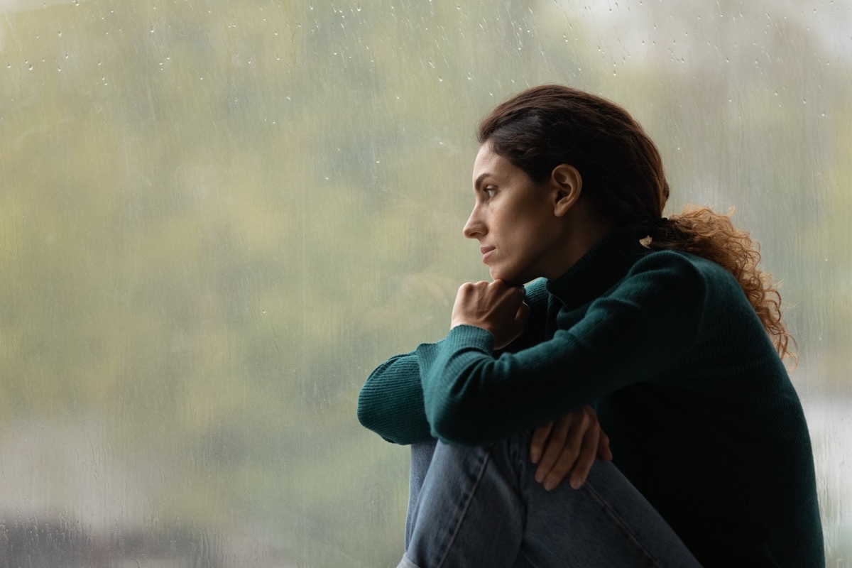 Woman sits by her window anxious.