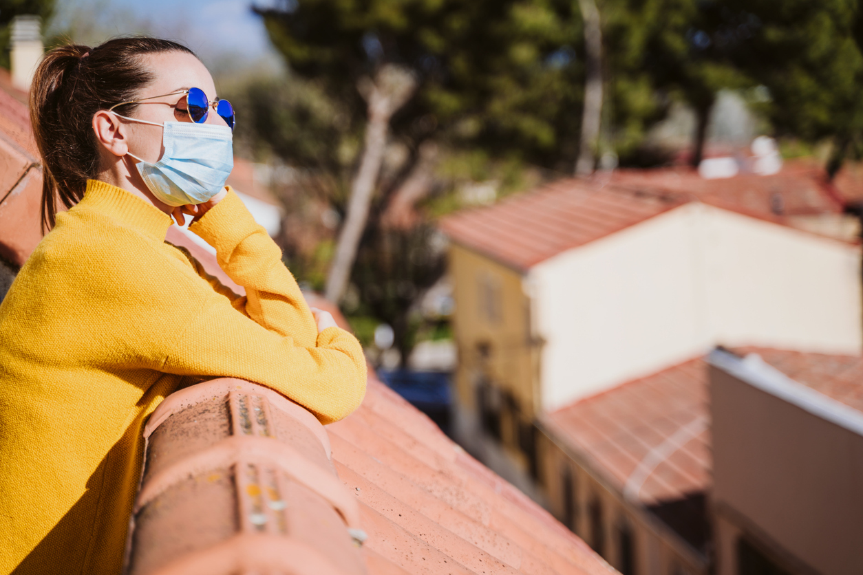 A young woman standing in the sunlight on a balcony because the sun kills coronavirus