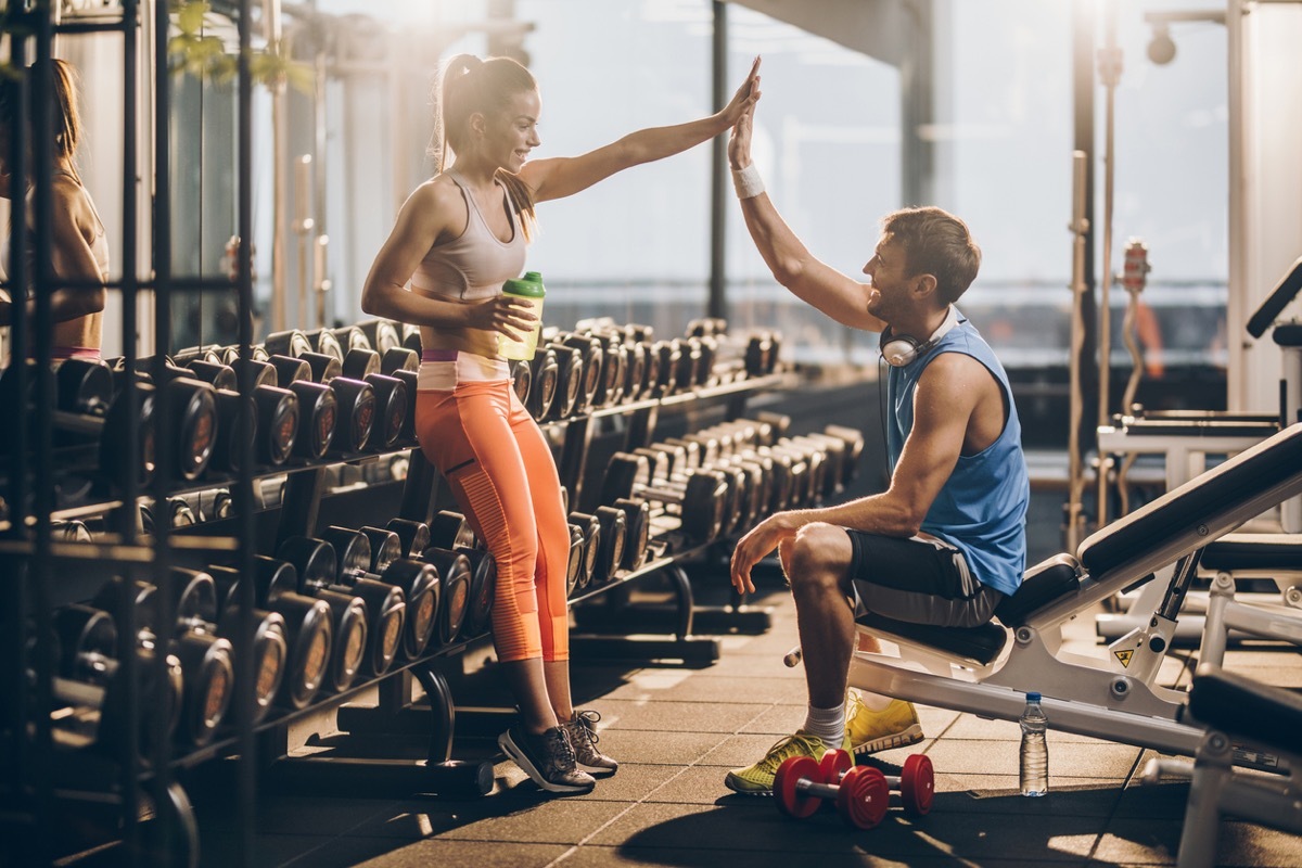 white woman and white man giving each other a high five by the weights at the gym