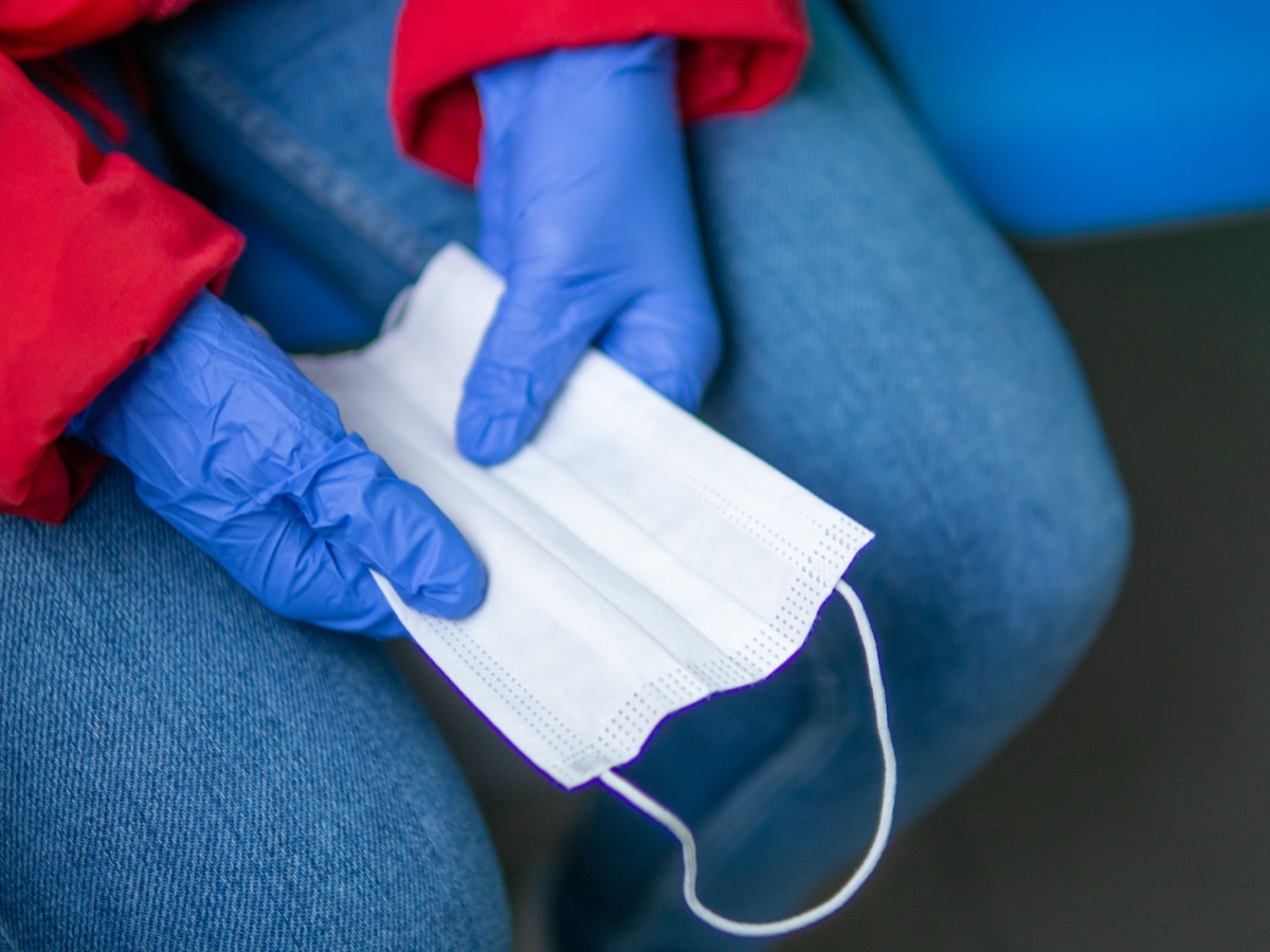 A woman hands in blue rubber gloves holding spare surgical mask protecting from viruses in public transportation