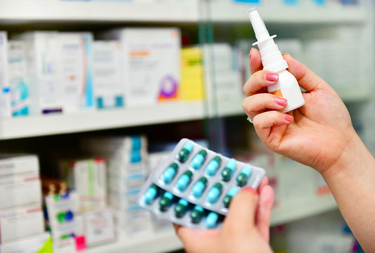 A person holding pills and a nasal inhaler at the pharmacy