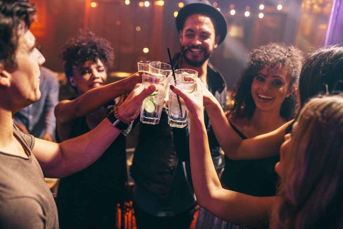 Group of friends having drinks at the night club party. Young people enjoying at a bar toasting cocktails.