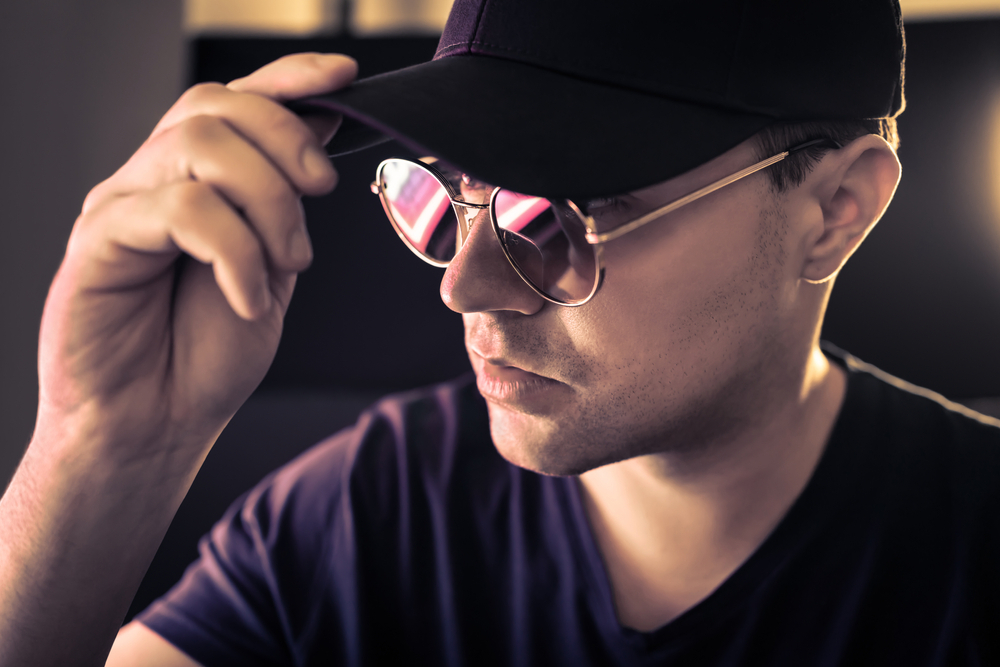 A man putting on a hat and sunglasses as part of a disguise