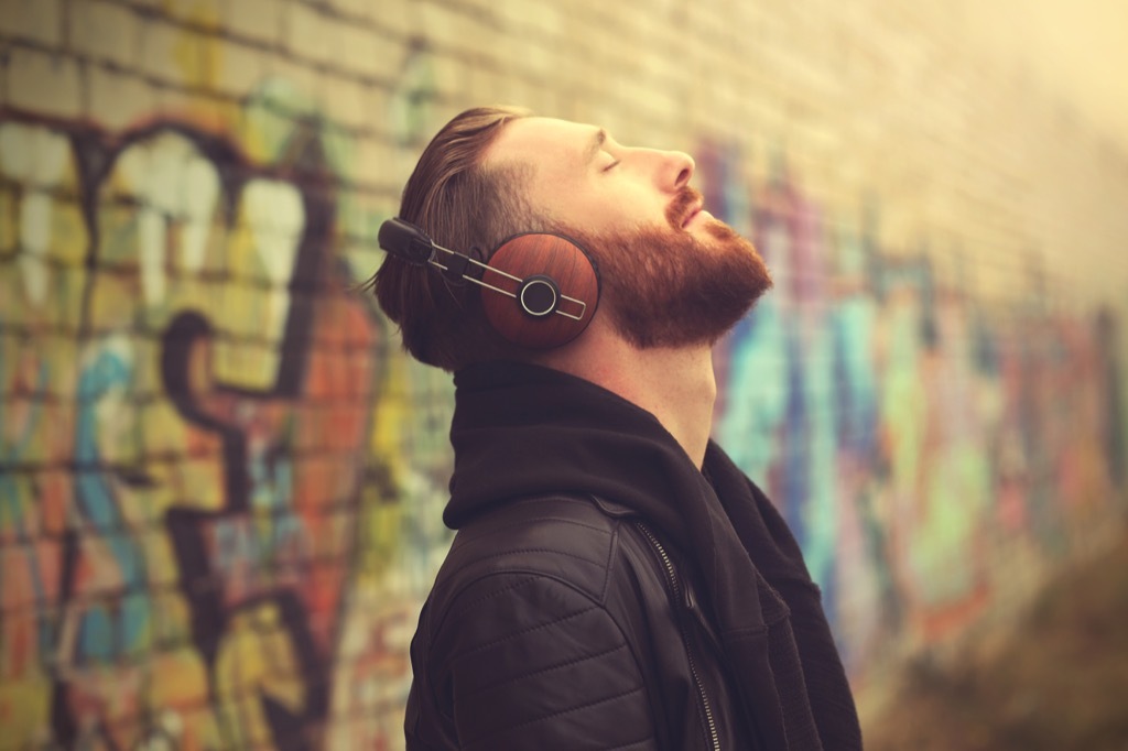 man listening to music on headphones outside in front of a brick wall