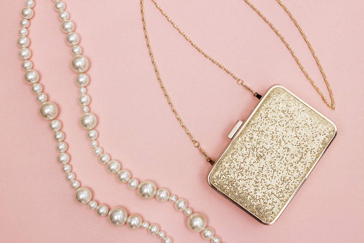 Golden purse and pearl necklace on pink background