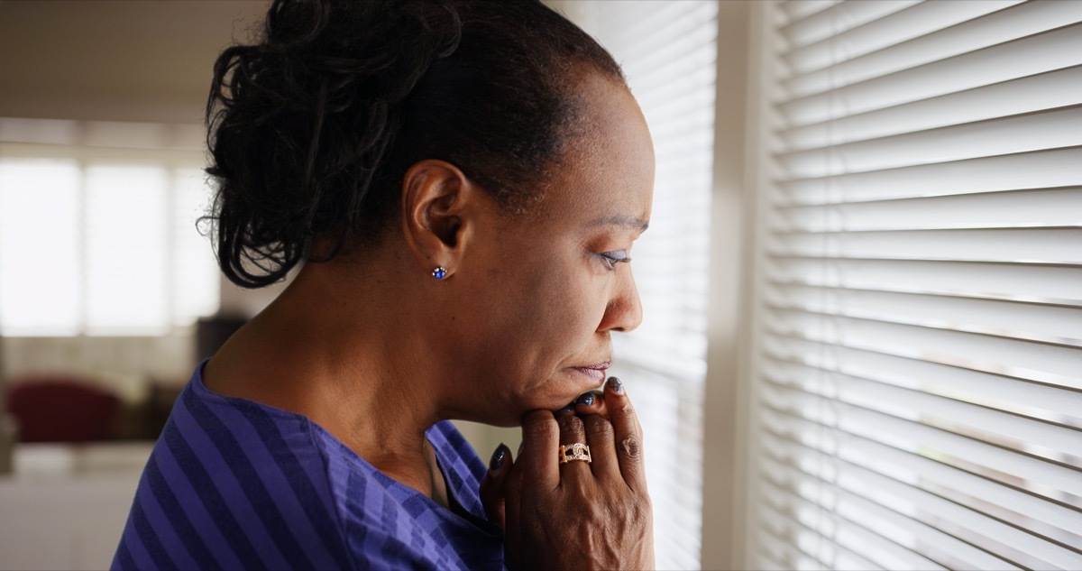 older woman looking out window looking sad