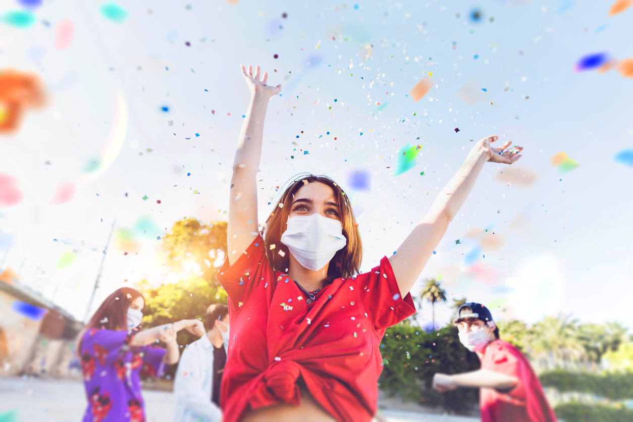 A group of young people wearing face masks celebrate outdoors with confetti