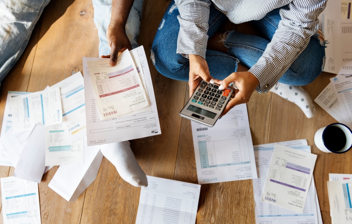 couple sitting on wooden floor with bills and calculator