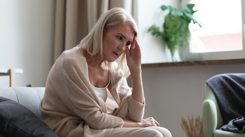 A senior woman sitting on the couch and holding her head with an anxious look