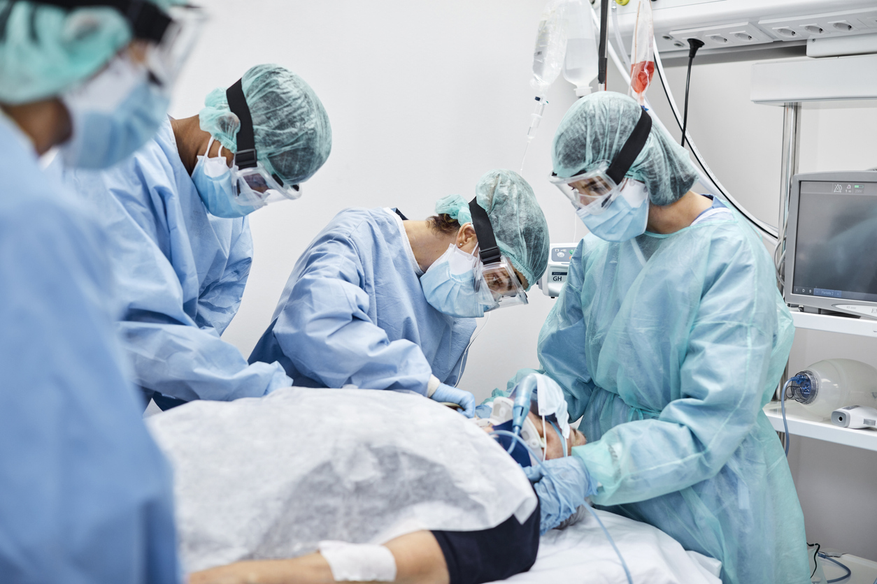 A patient suffering from COVID-19 is cared for by a team of doctors and nurses in the ICU who are all wearing protective gear.