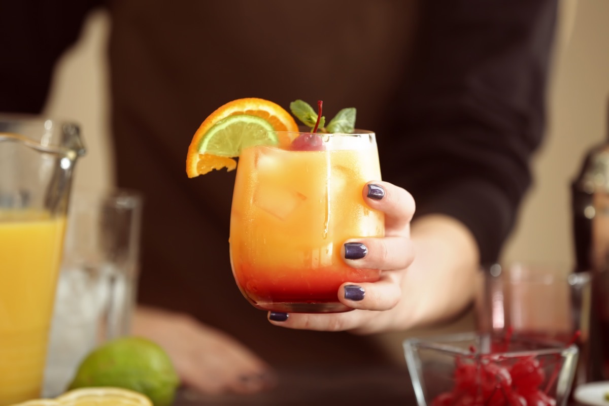 a woman holding glass of tequila sunrise cocktail