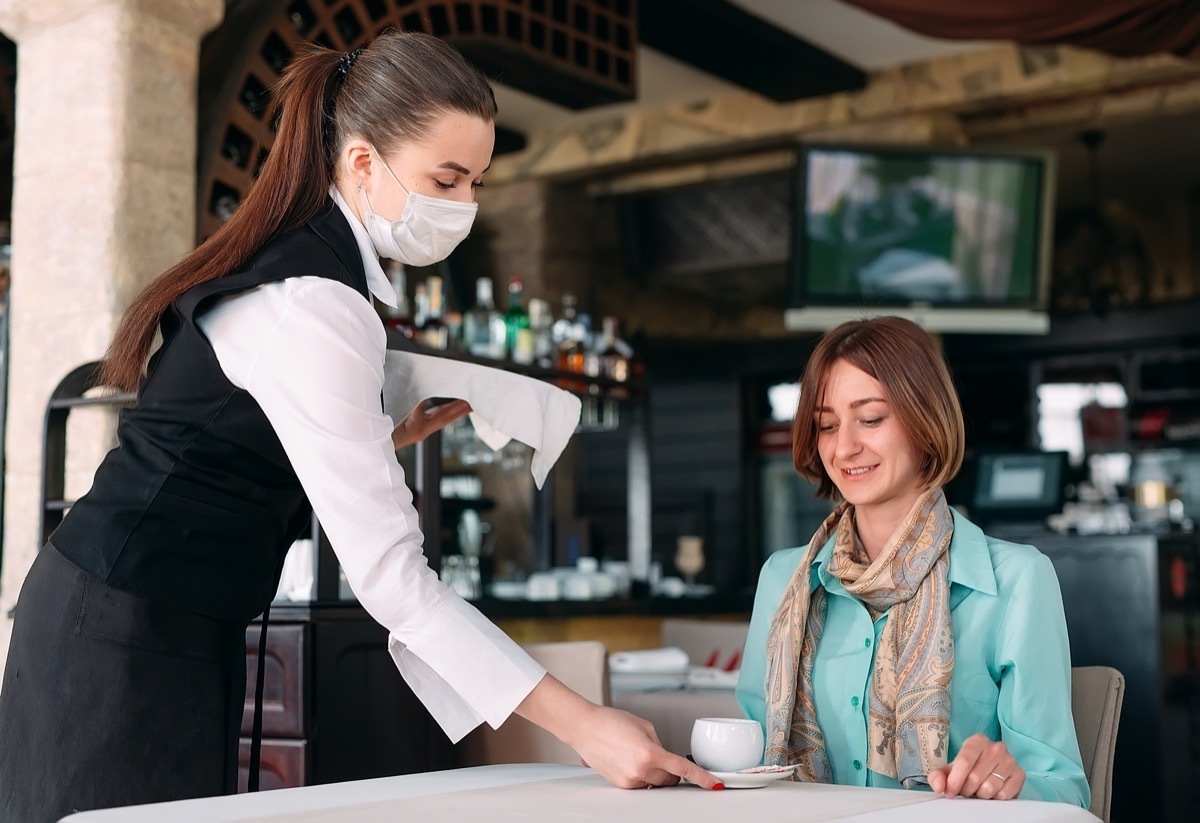 waiter in a medical mask serves coffee