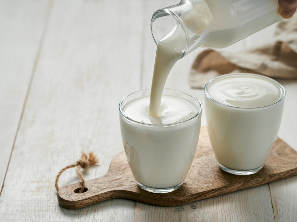 pouring milk, buttermilk or yogurt in glass, on wood