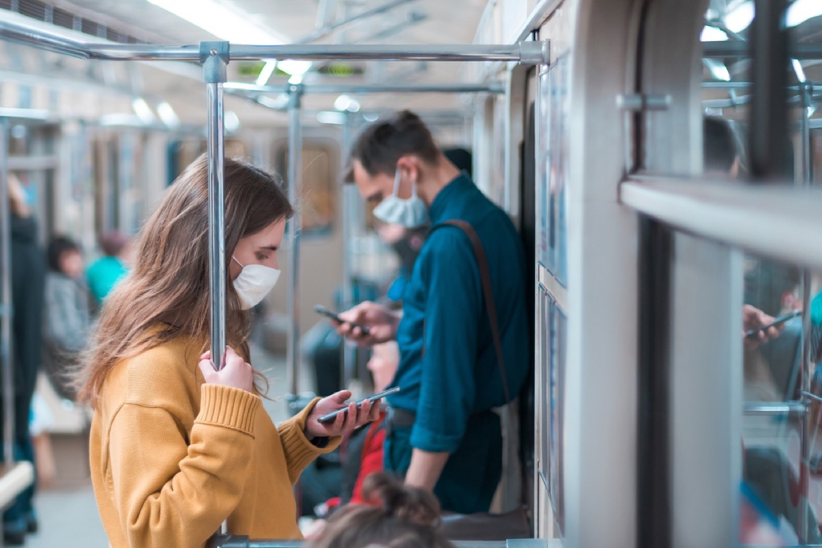 woman with face mask looking at her phone on subway with man in a face mask behind her