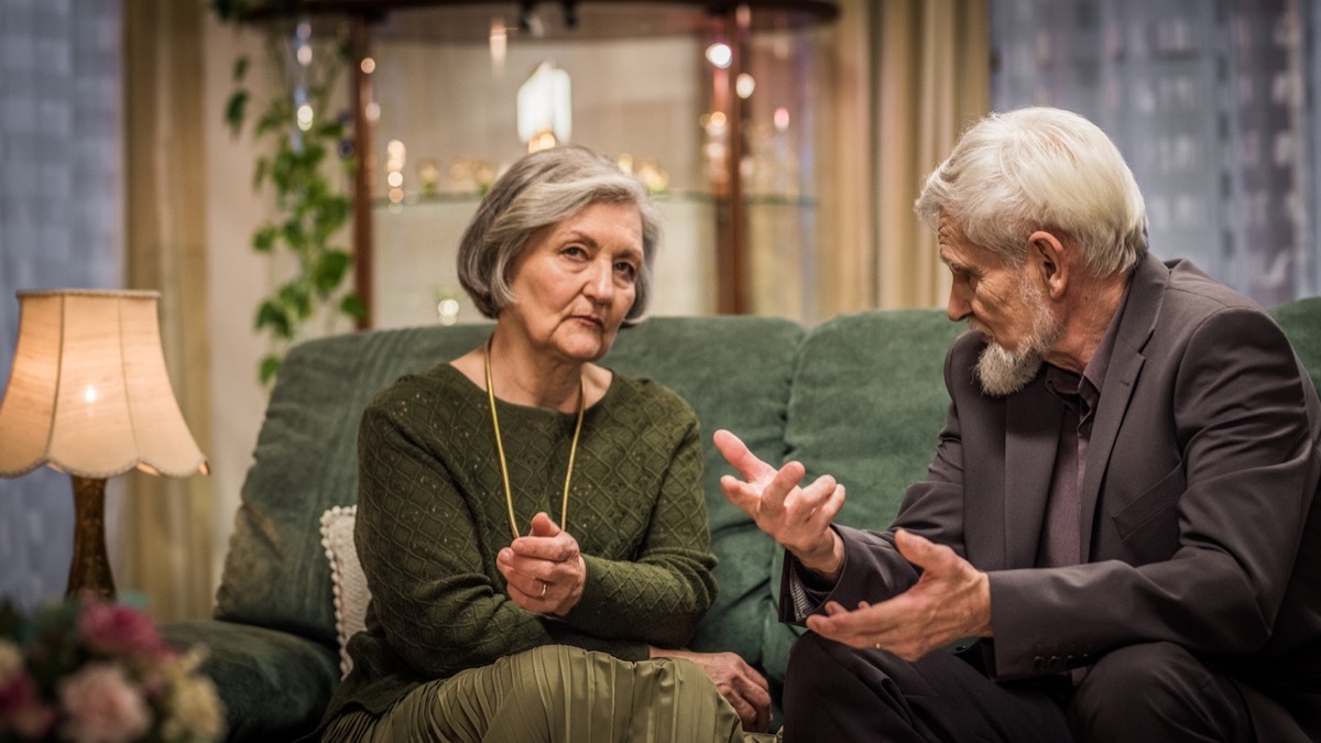 Elderly couple sitting on the living room sofa and having a serious conversation.