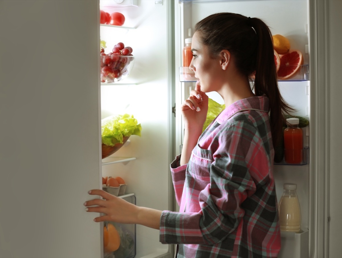 Young woman looking into fridge at night