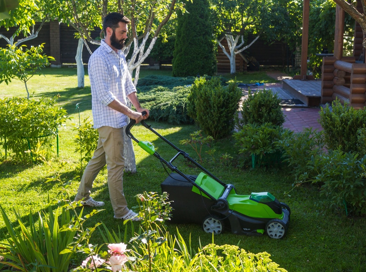 Young man mowing the lawn in the garden. Mowing the lawn on country house