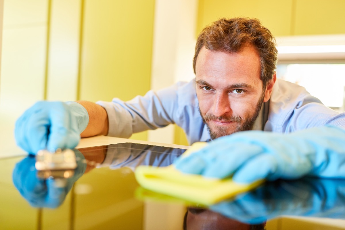 Man cleaning stovetop with cloth and scrapper