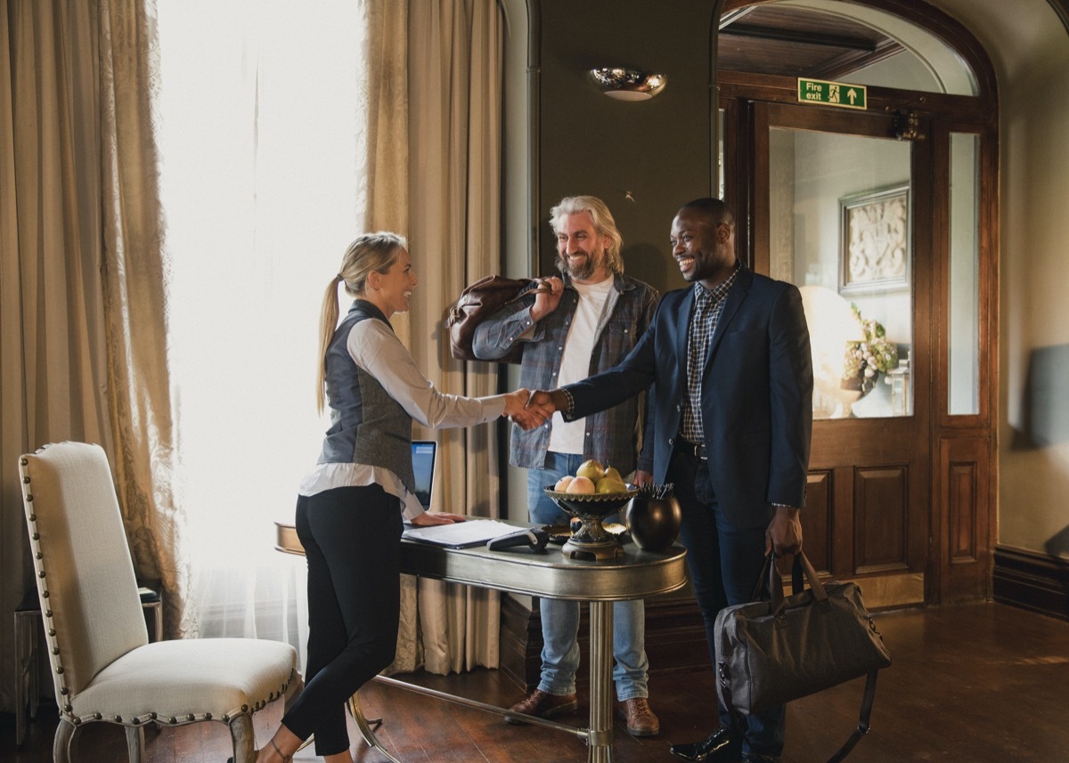 Two men arrive at their luxury hotel where they are staying. They greet the hotel receptionist and pay for their stay.