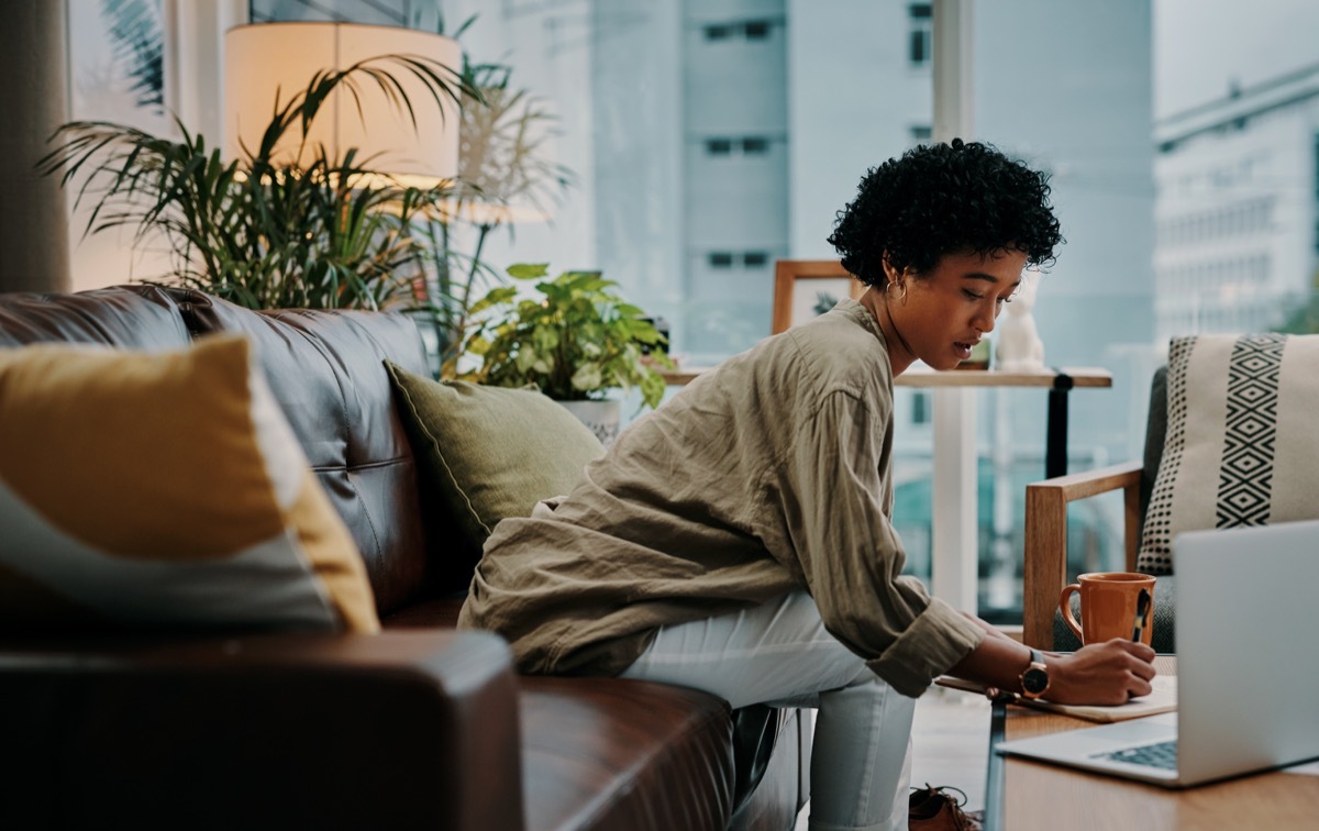 Shot of a woman making notes while using her laptop at home