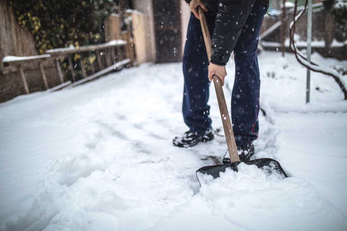 Senior man with a shovel cleaning snow from his back yard at his house.