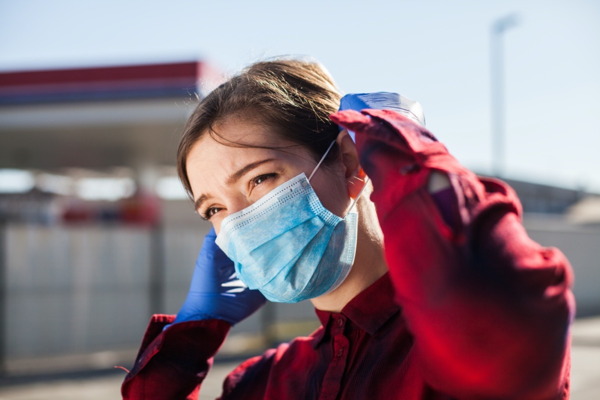 woman adjusting protective face mask,standing on petrol station parking lot