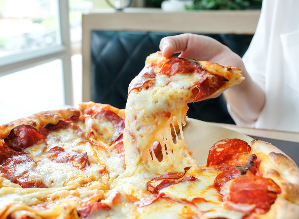 Woman grabbing slice of cheese pizza with pepperoni meat lovers