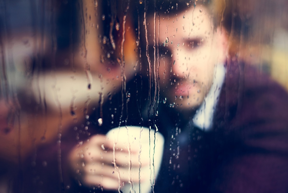 contemplative man holding a cup of coffee looking out a rainy window {stereotypes}