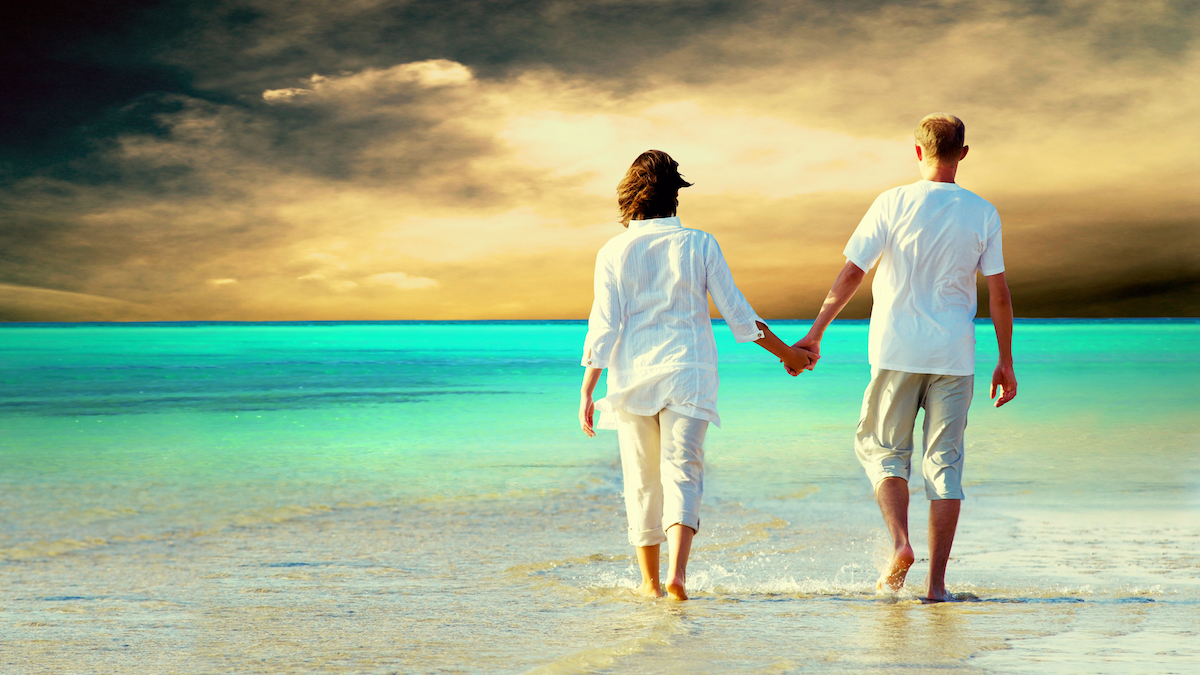 Rear view of a couple walking on the beach, holding hands.