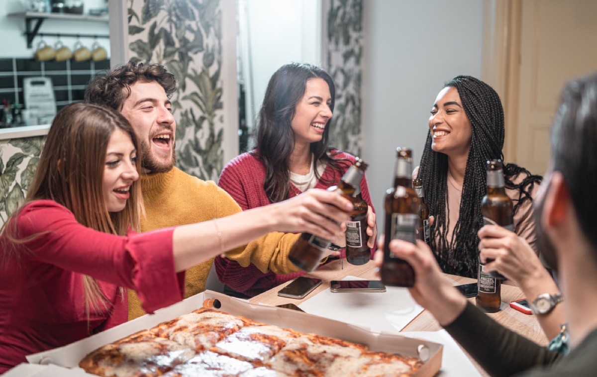 group of young people toasting beer and eating pizza