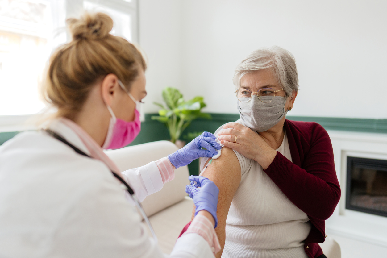 A senior woman receiving a COVID-19 vaccination from a female healthcare worker