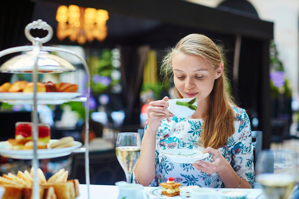 Beautiful young woman enjoying afternoon tea with selection of fancy cakes and sandwiches in a luxury Parisian restaurant