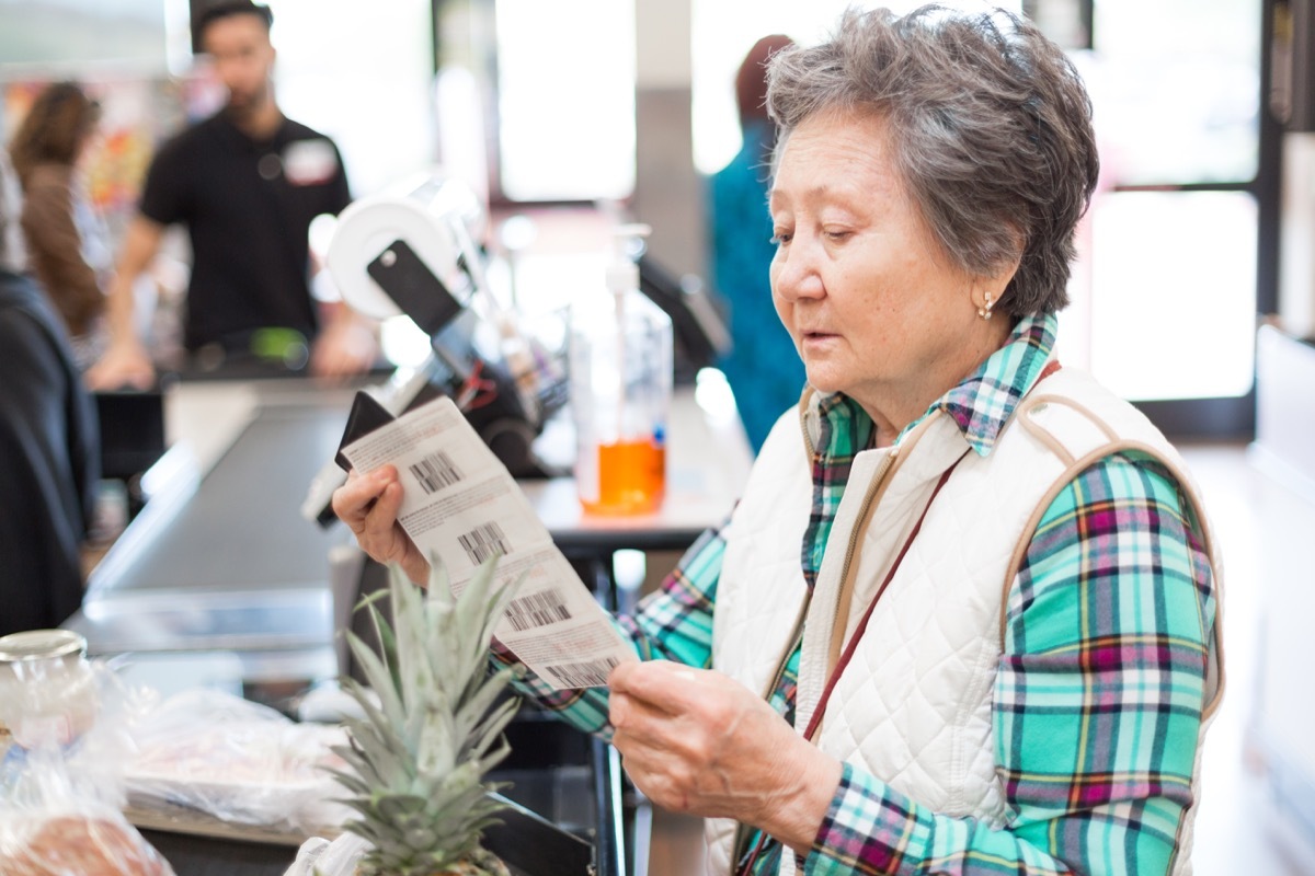 Prudent senior woman looking at her coupons before paying for her groceries.